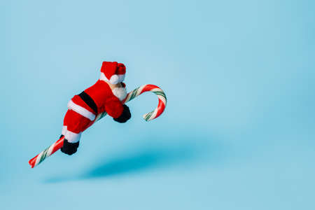 Santa Claus flying on candy cane against pastel blue background. Creative Christmas or New Year celebration concept. Winter holidays empty banner.の写真素材