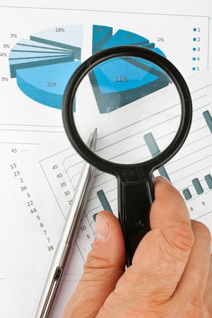 Hand with magnifying glass on a background of diagramsの写真素材