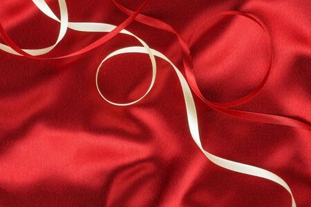 Red and white ribbon on a red silk, as backgroundの写真素材