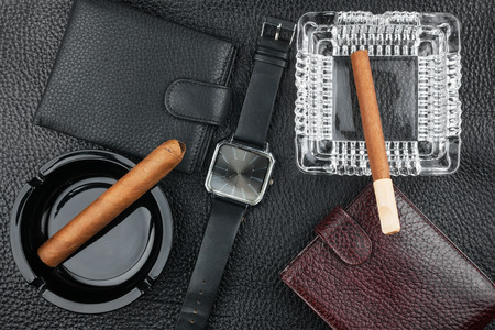 Two ashtray with cigars, two purses and watches on the natural leather, luxury background