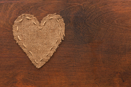 The symbolic heart of burlap lies on a wooden surface, as a backgroundの写真素材