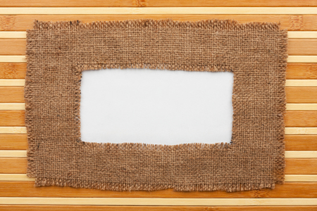 Frame made of burlap with white background lying on a bamboo mat, with space for your textの写真素材