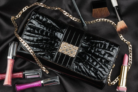 Beautiful bag from patent leather and cosmetics lying on black satin, as backgroundの写真素材