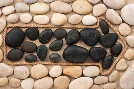 Pointer made of rope with white and black stones, lying on the sandの写真素材