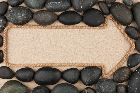Pointer made of rope with  black stones, lying on the sandの写真素材