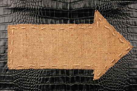 Arrow made of burlap lies on a crocodile skin, with place for your textの写真素材