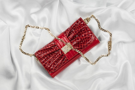Red lacquer bag lying on a white silk, as backgroundの写真素材