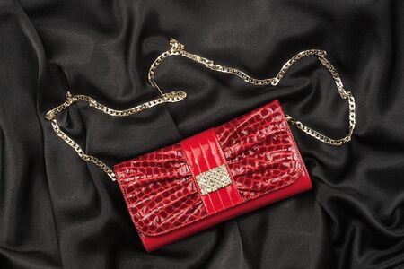 Red lacquer bag lying on a black silk, as backgroundの写真素材