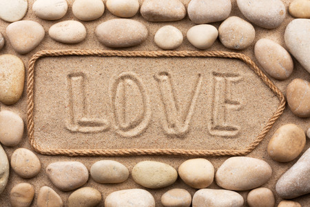 Pointer made of rope with an inscription love  with white stone, on sandの写真素材