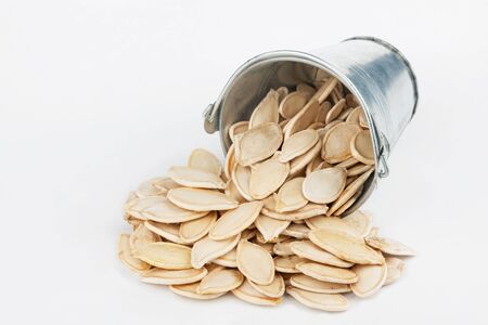 Pumpkin seeds spilling out of bucket, on a white backgroundの写真素材