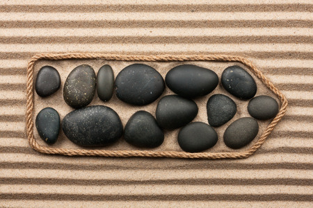 Pointer made of rope with black stones, lying on the striped sandの写真素材