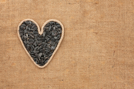 Heart made from rope with sunflower seeds lying on sackcloth, with space for textの写真素材
