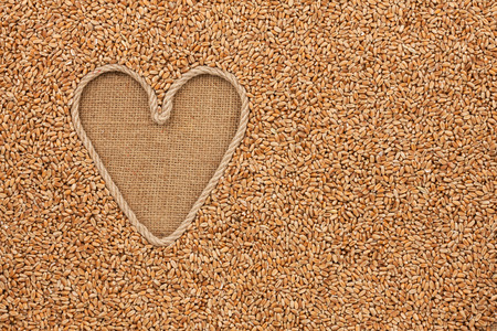 The symbolic heart made of rope lies on sackcloth and wheat grains, with space for your textの写真素材