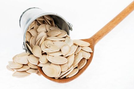 Bucket of pumpkin seeds crumbles in the a wooden spoon, on a white backgroundの写真素材