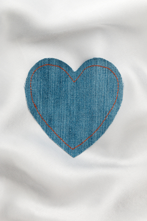Heart made of denim fabric with yellow stitching on white silk, with space for your text