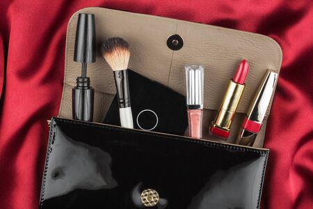 Fashion concept. Black patent leather bag  with cosmetics, on red backgroundの写真素材