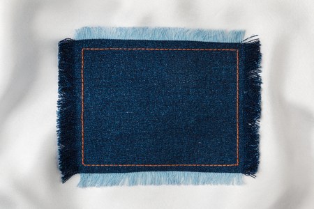 Frame for the text from a blue jeans fabric with the stitched lines of an orange thread and fringed, on a white silkの写真素材
