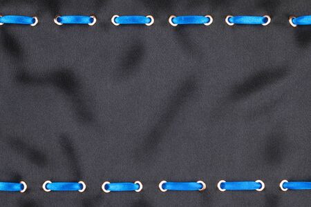 Blue satin ribbon inserted in the gold rings on black silk, trendy background