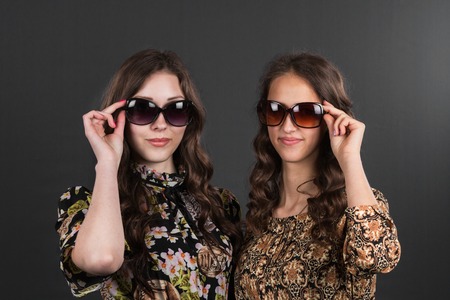 Two beautiful happy girls in sunglasses on the grey background. Young active people.