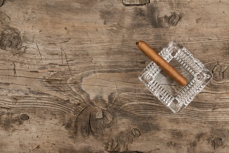 Glass ashtray with cigar stands on a wooden surface, can be used as backgroundの写真素材