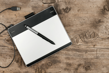 Graphics tablet with stylus lying on a wooden surface, top view with space for your textの写真素材