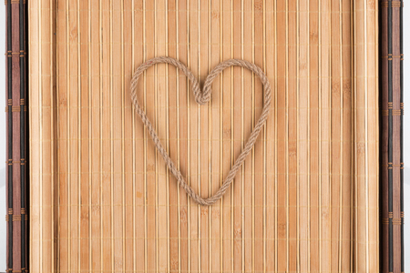 Symbolic heart made of rope lying on a furled bamboo mat, as background, conceptual imageの写真素材