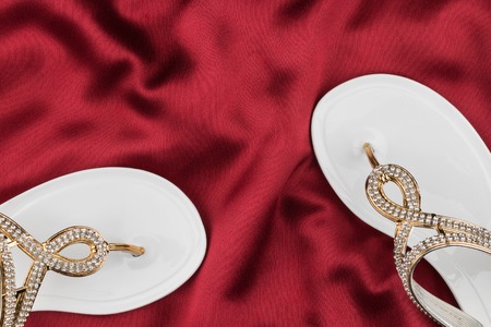 Couple beach white flip flops encrusted with rhinestones standing on the crumpled red silk, with space for your textの写真素材