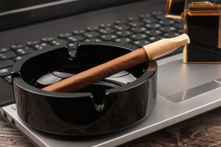 Close-up cigar in the ashtray standing on a laptop. Habits personの写真素材