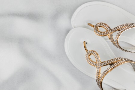 Pair beach white sandals in rhinestones standing on white silk. View from aboveの写真素材