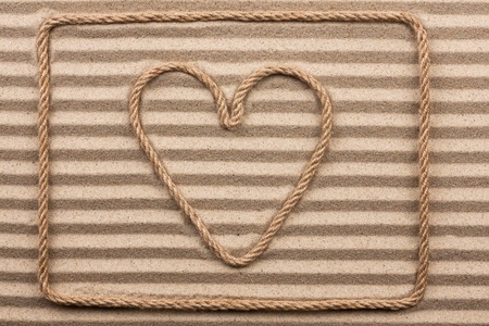 Heart made of rope lies on wavy sand. View from aboveの写真素材