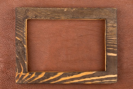 Rectangular frame made of dark wood lies on brown natural leather. Texture of a tree. View from above.の写真素材