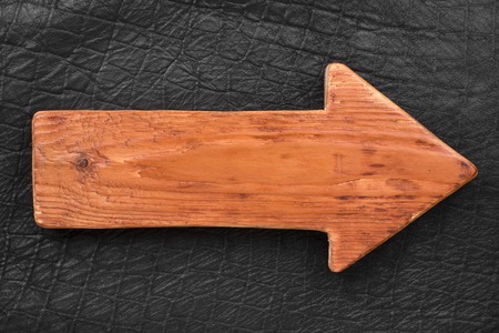 Wooden pointer made of light wood with a place for your text. Arrow lying on black leatherの写真素材