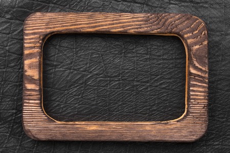 Beautiful wooden frame cut from a dark board, lies on a black leather. View from aboveの写真素材