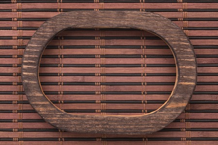 Beautiful wooden frame cut from a solid dark board, lies on a dark bamboo mat. View from aboveの写真素材