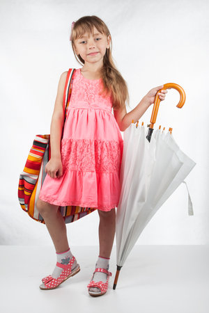 Cute little girl with umbrella and bag on her shoulder posing on a white background. Fashion portrait of girl child.の写真素材
