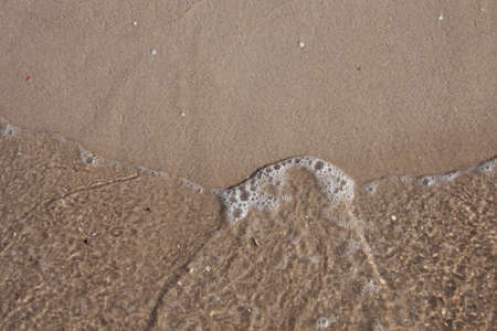 Close-up of a sea wave on a sandy beach. Top view. Sand beach texture. White foam sandy seashore top view.の写真素材