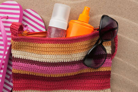 Beach accessories on the sand. Bag, colorful flip flops and bag, sunscreen and sunglasses. Summer vacation. Top viewの写真素材