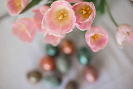 Beautiful colored shiny easter eggs on the white plate. Pink tulips flowers bouquet. Happy easter concept.の写真素材