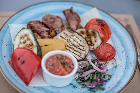 BBQ and grilled vegetables with salsa sauce on the beautiful blue plate in the restaurant. Minsk, Belarus.の写真素材