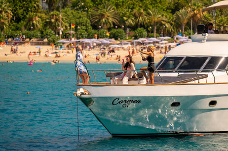 Alanya, Antalya, Turkey. 18 july 2023. Three young beautiful women takes a photo and selfy on modern yacht boat at sea on tropical sand beach background.のeditorial素材