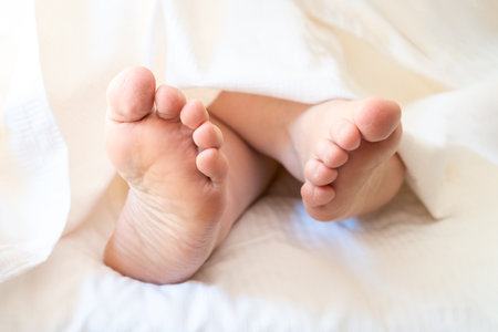Close-up woman feet alone in white bed, on a white sheet under a white blanketの写真素材