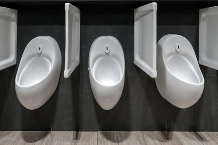 Three white urinals in public black toiletの写真素材