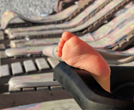 children's foot sticking out of the wheelchair, with sun loungers on the beach in the backgroundの写真素材