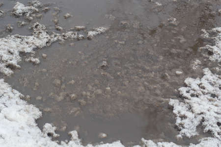 Winter puddles and snow slush on road.の写真素材