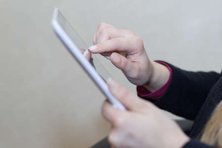 A girl holds in her hands and uses a tablet computer close up