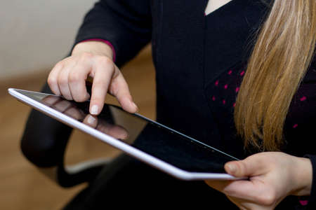 A girl holds in her hands and uses a tablet computer close up