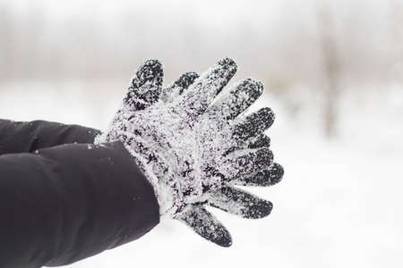 Female hands in black gloves in the snow close up.の写真素材