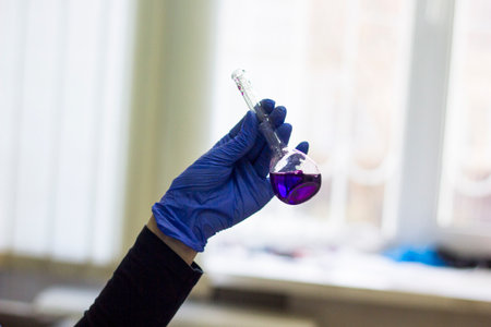 A gloved hand holds a vial with a purple solution