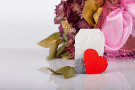Close-up of tea bag with red heart tag onon floral background