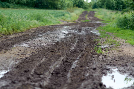 Ukrainian rural landscape with empty countryside dirt road after rains in summer day. Slush on broken rural road with deep tire tracksの写真素材